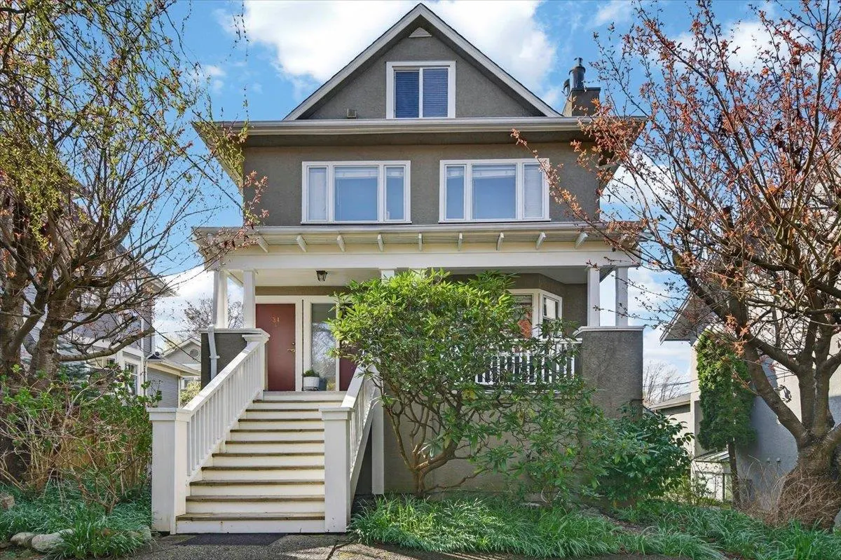 Two-story gray house with white trim, a front porch, and a long staircase leading to two red front doors.