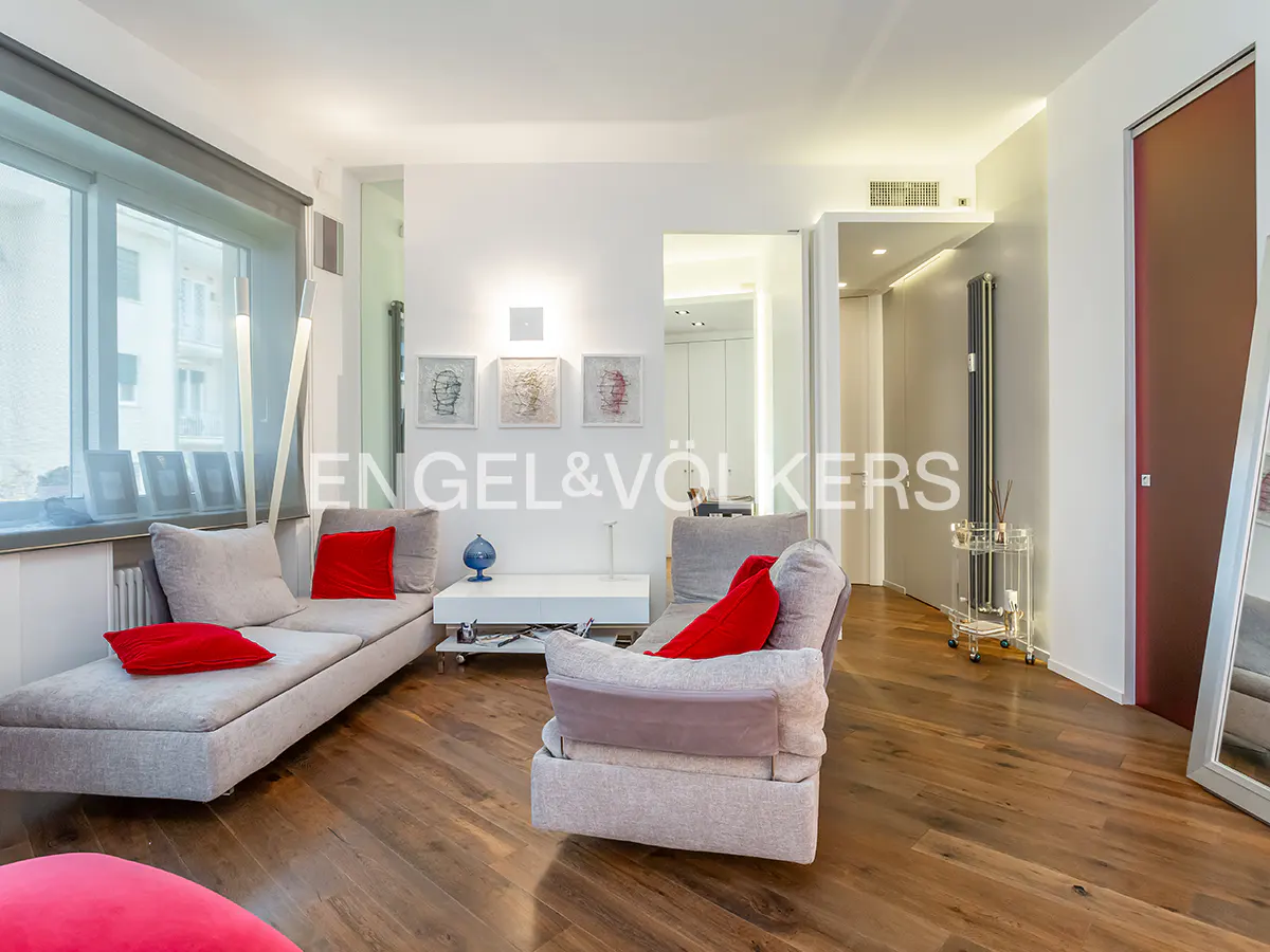 Bright living room with hardwood floors, gray sofas with red pillows, and Engel & Völkers logo.