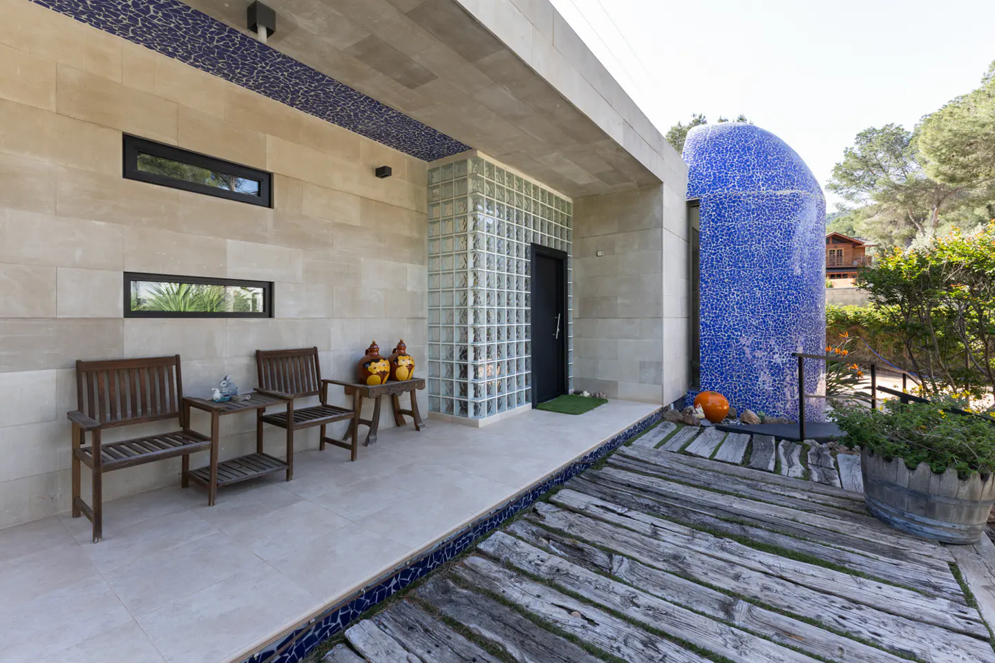 Exterior view of a modern home with a blue mosaic dome, stone walls, and wooden benches on the patio.