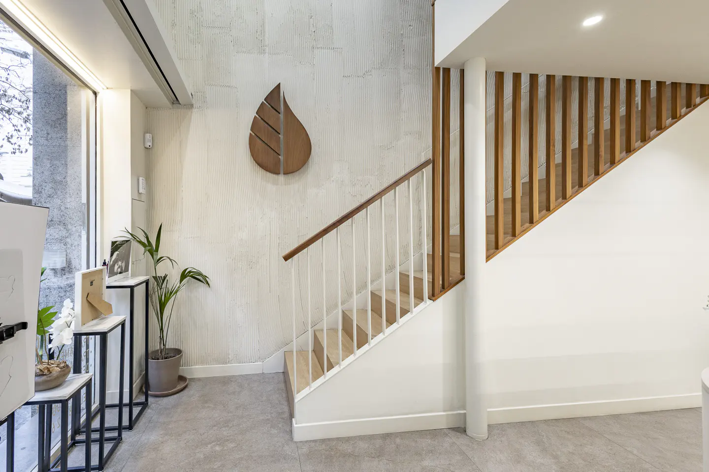 Interior view of a modern staircase with wood railings and a leaf-shaped wall decoration in a bright, minimalist space.