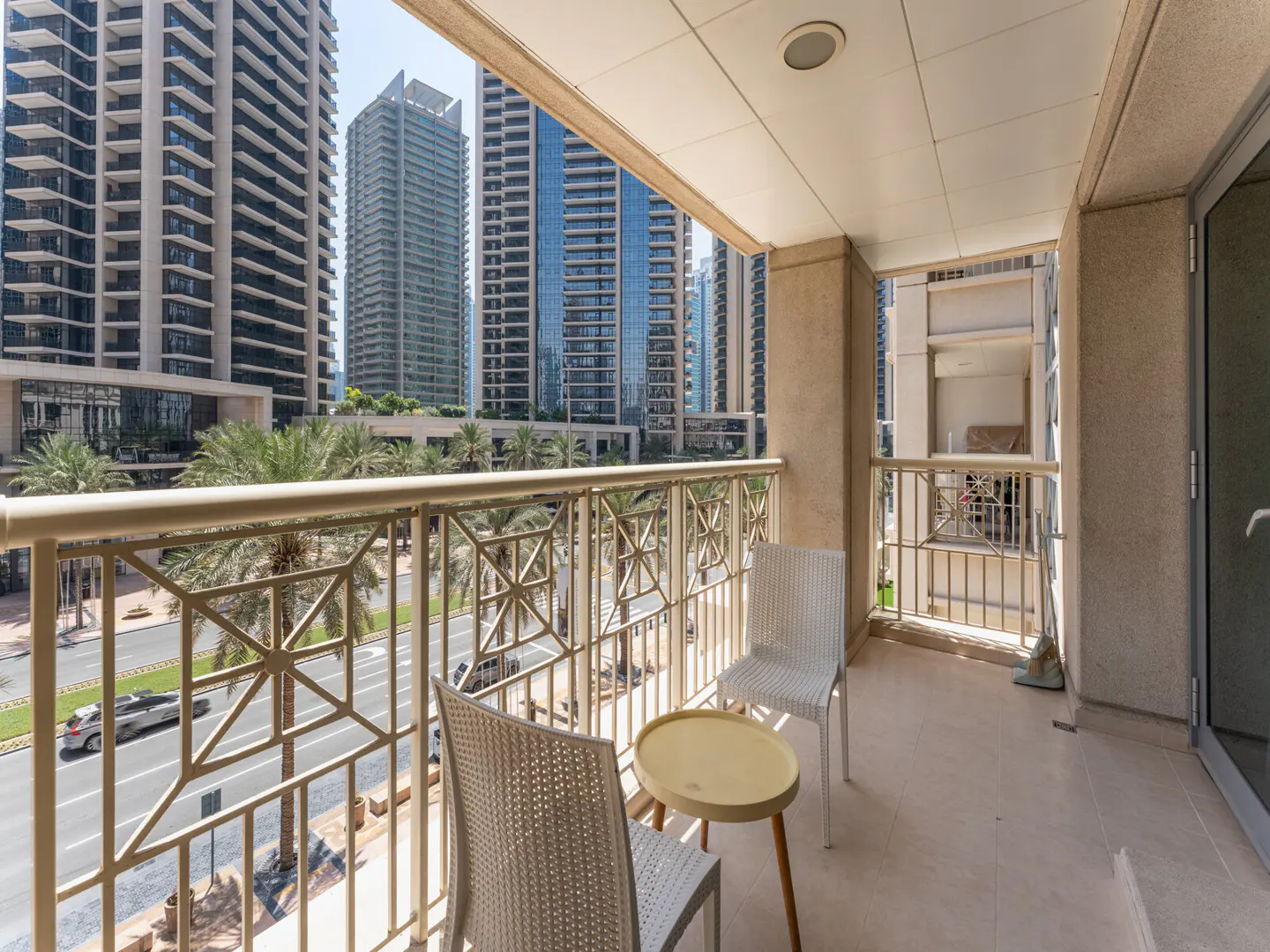 Balcony view with two white chairs and a small yellow table. Tall buildings and palm trees are visible in the background.