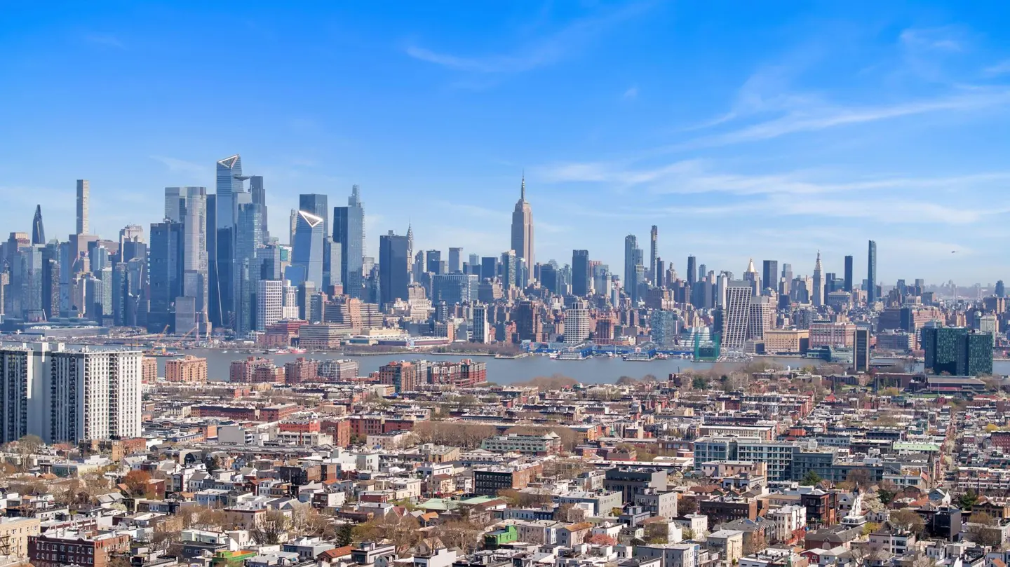 Cityscape view of New York City with the Empire State Building under a blue sky, seen from a residential area.