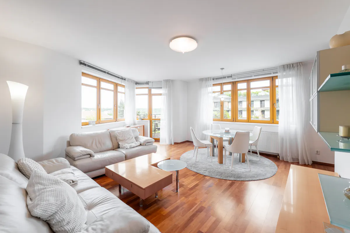 Bright living room with hardwood floors, white sofas, a wooden coffee table, and a dining area with a round table and chairs.