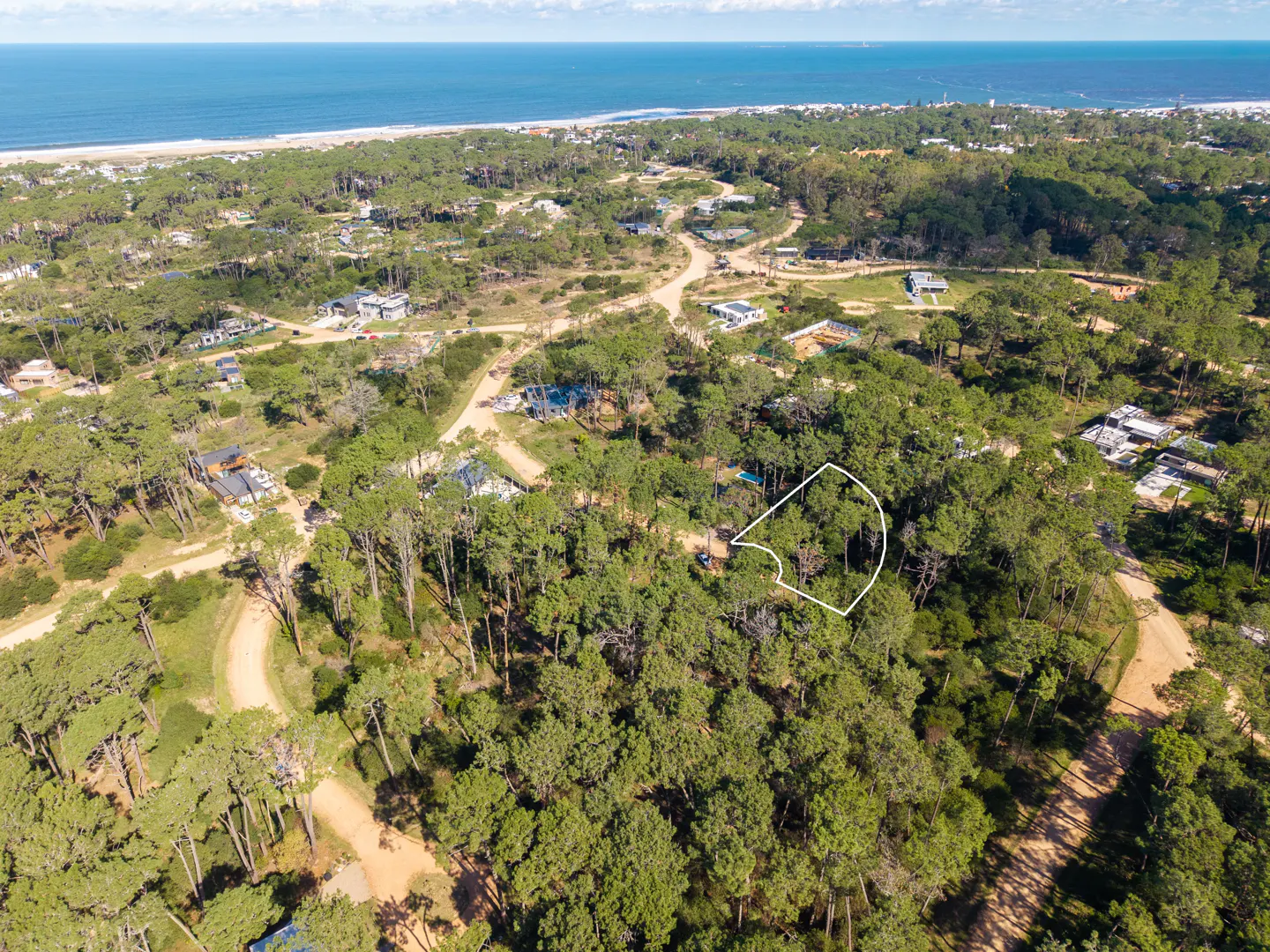 Aerial view of a wooded lot outlined in white, near a beach and ocean.