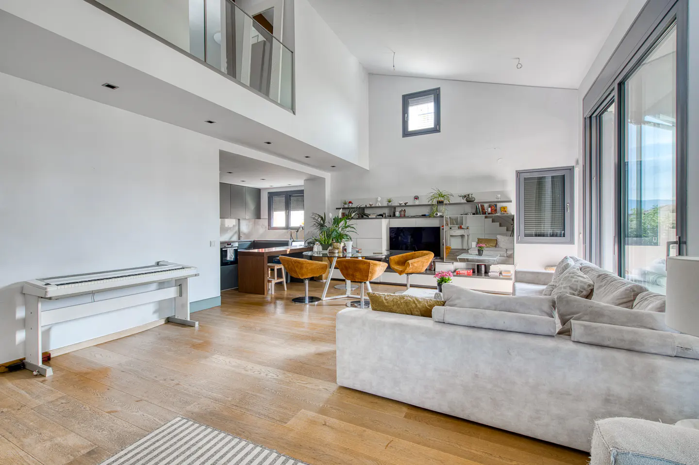 Modern open-plan living room with white walls, light wood floors, a large grey sofa, and a dining area with yellow chairs.