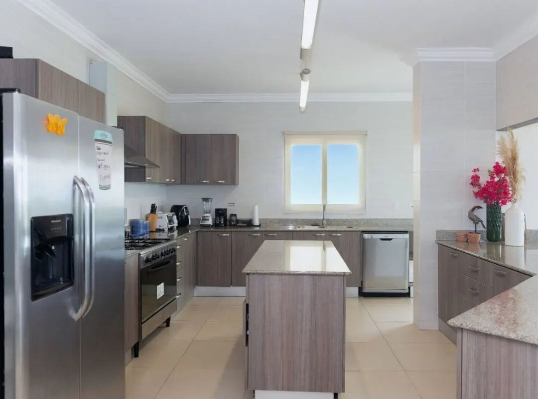 A modern kitchen with gray cabinets, stainless steel appliances, and a central island. A window lets in natural light.