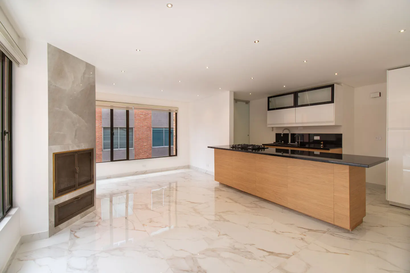 Bright, open-concept living space with marble floors, a fireplace, and a kitchen island with a black countertop.
