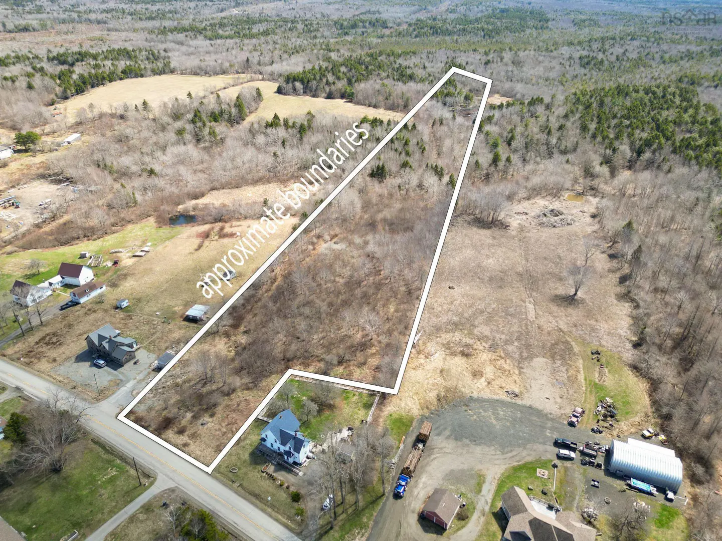 Aerial view of a vacant lot with approximate boundaries outlined in white, surrounded by trees, fields, and houses.