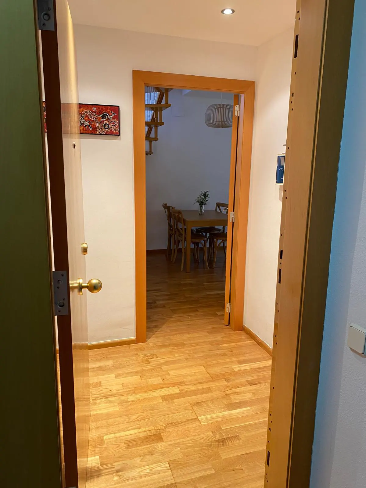 View through doorway to dining room with wood table, chairs, and stairs. Wood floors and orange trim.