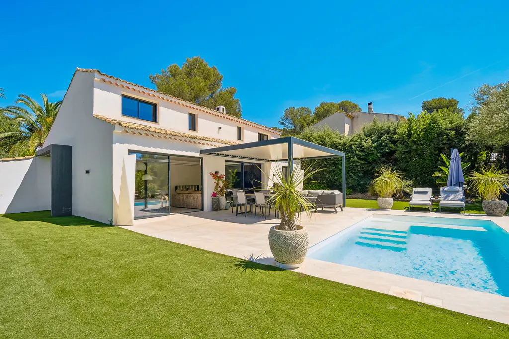 A white two-story house with a pool, patio, and green lawn under a clear blue sky.