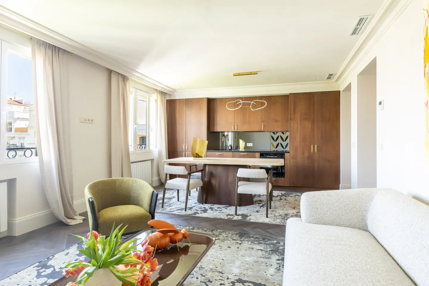 Modern living room with a white sofa, olive green armchair, and a dining area featuring wood cabinets and a stone table.