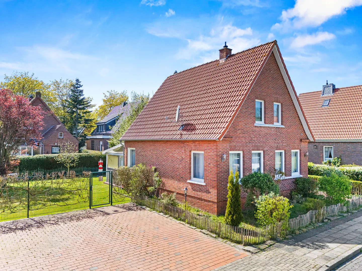 A two-story brick house with a red tile roof, white trim, and a brick driveway on a sunny day.