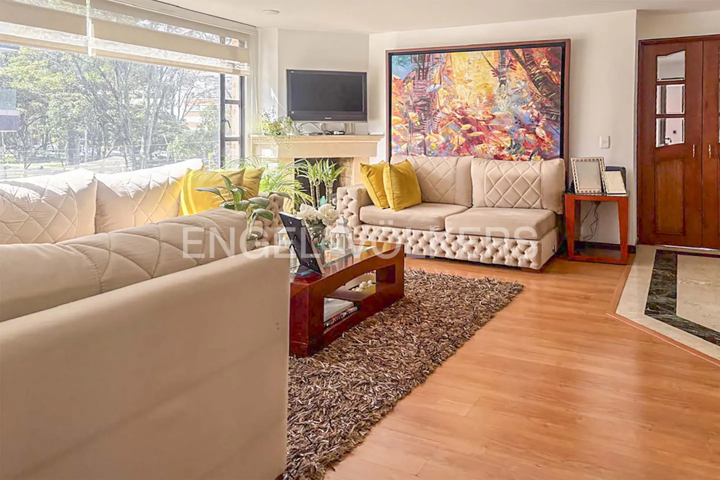 Living room with beige sofas, yellow pillows, a brown rug, and a colorful painting above the sofa.