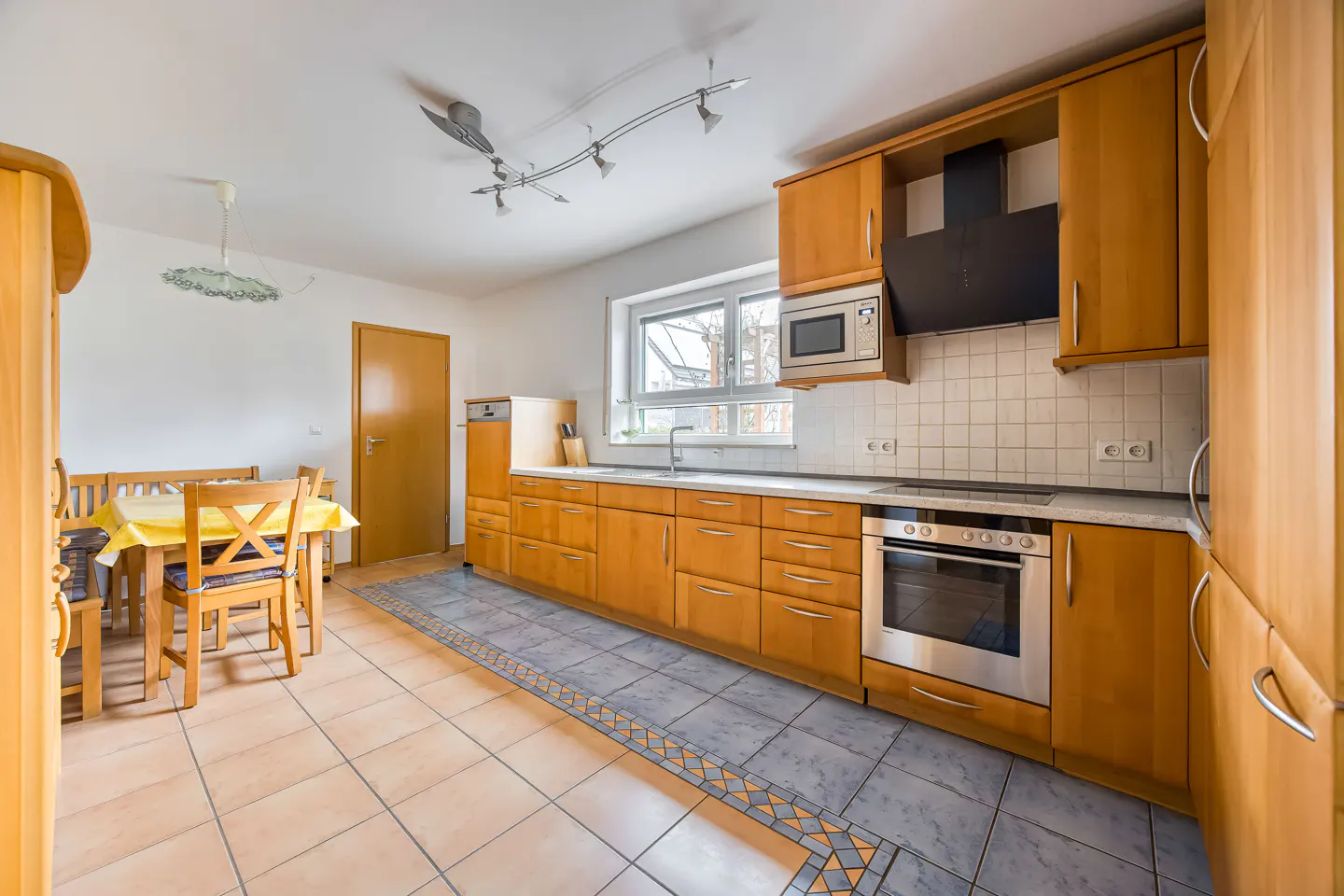Bright kitchen with wood cabinets, stainless steel appliances, and a dining table with a yellow tablecloth.