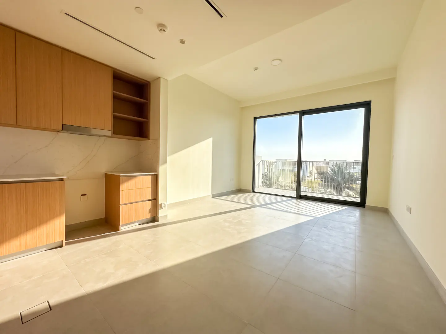 Bright, empty apartment with light wood cabinets, marble backsplash, and sliding glass doors to a balcony.