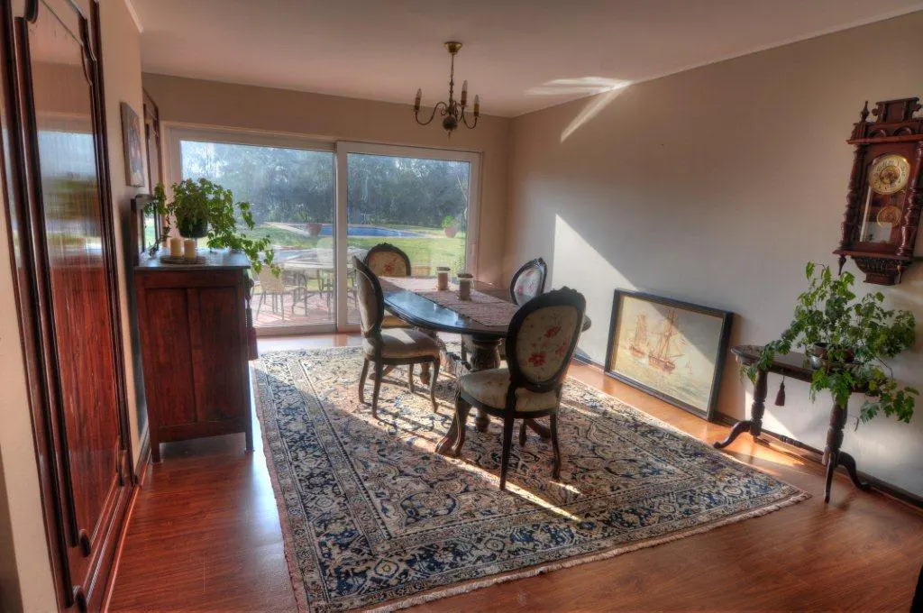 Sunlit dining room with a dark wood table, floral chairs, and a patterned rug on hardwood floors. A sliding glass door leads to a green yard.
