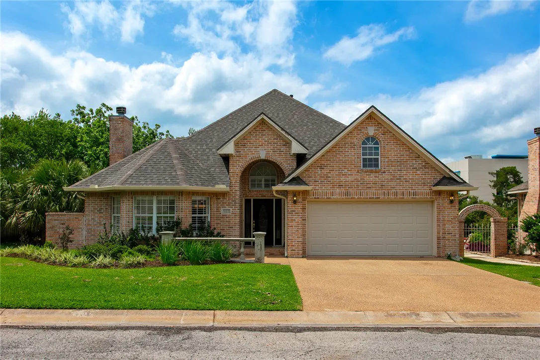 A single-story brick house with a gray roof, a two-car garage, and a green lawn under a blue sky.