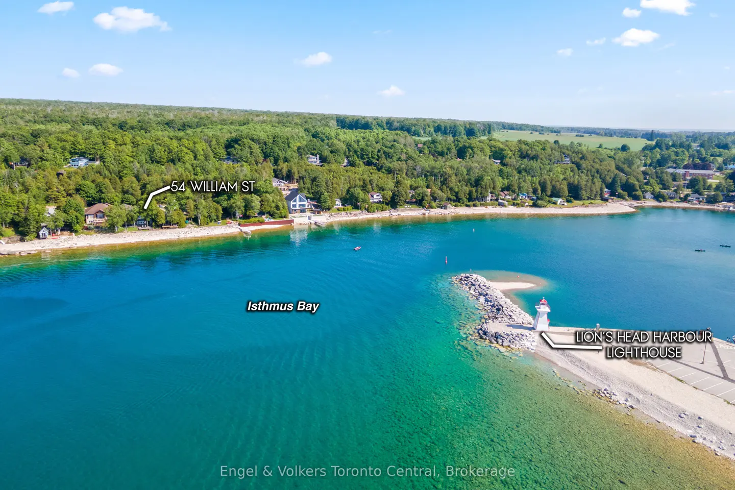 Aerial view of Isthmus Bay with turquoise water, a lighthouse on a pier, and lush green trees along the shoreline.