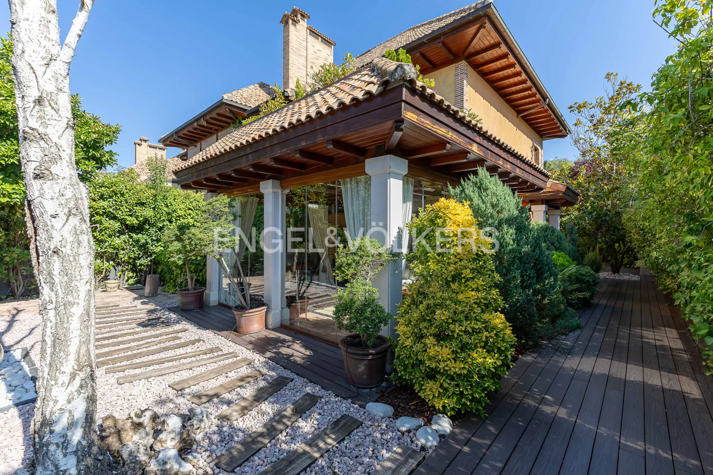 Exterior view of a two-story house with a tile roof, a covered porch with white columns, and lush landscaping.