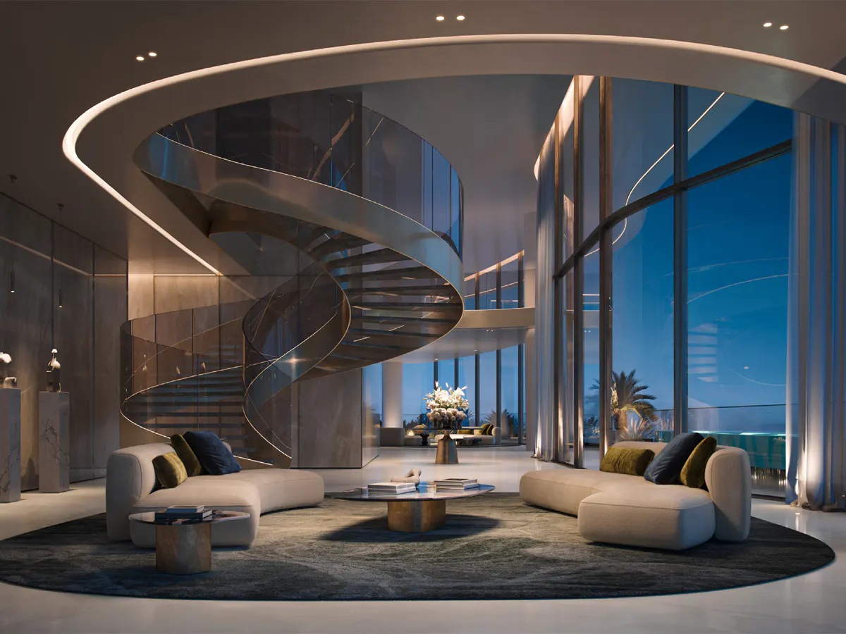 A modern living room with curved white sofas, blue and green pillows, and a spiral staircase. Large windows offer a view of the ocean at dusk.