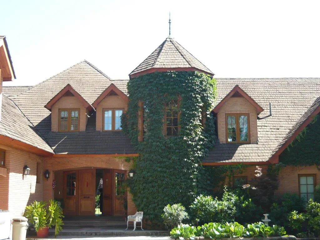 Exterior view of a brick house with a turret covered in green ivy, a brown shingle roof, and a wooden door.