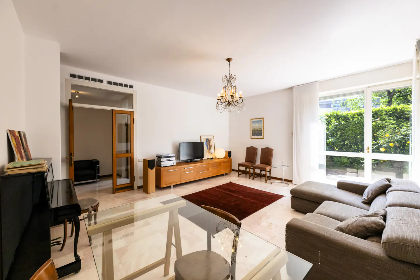 Bright living room with a piano, brown sectional sofa, glass table, and a wooden TV stand with a TV.