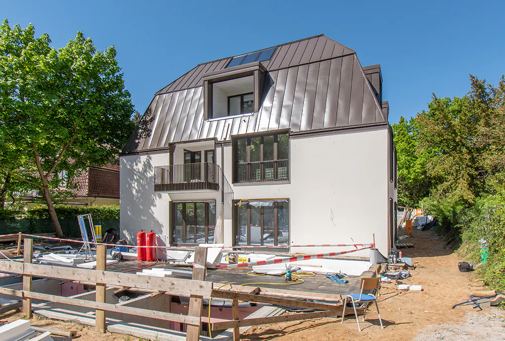 New construction home with a brown metal roof and white exterior walls. The yard is under construction with tools and equipment.