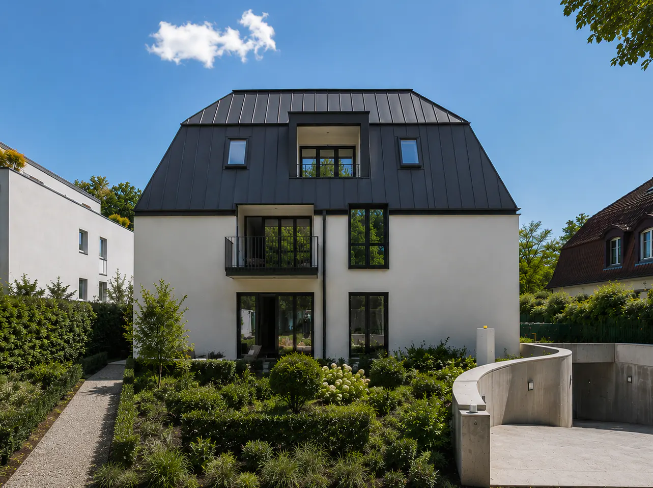 Modern white building with a black roof, windows, and balcony. Green landscaping and a curved driveway lead to a garage. Blue sky.
