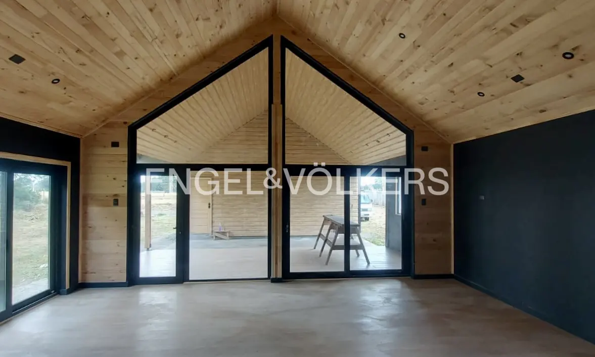 A bright room with wood walls and ceiling, black trim windows, and a concrete floor. The Engel & Völkers logo is superimposed.