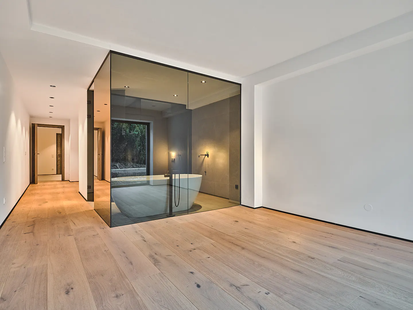 Modern bathroom with wood floors, white walls, and a glass-enclosed tub area.