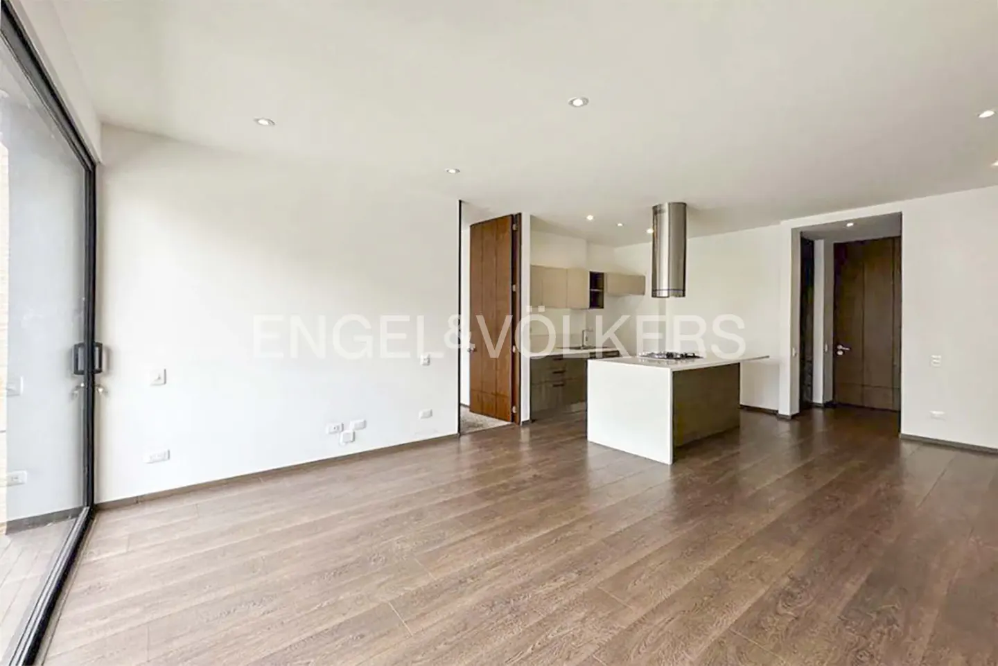 Open-concept living space with hardwood floors, white walls, and a kitchen island. Engel & Völkers logo visible.