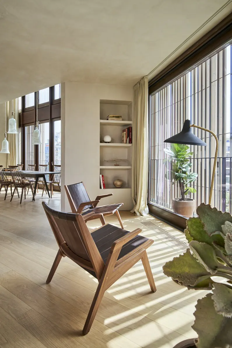A bright, modern living room with two wooden chairs, a dining table, and a large window with a view.