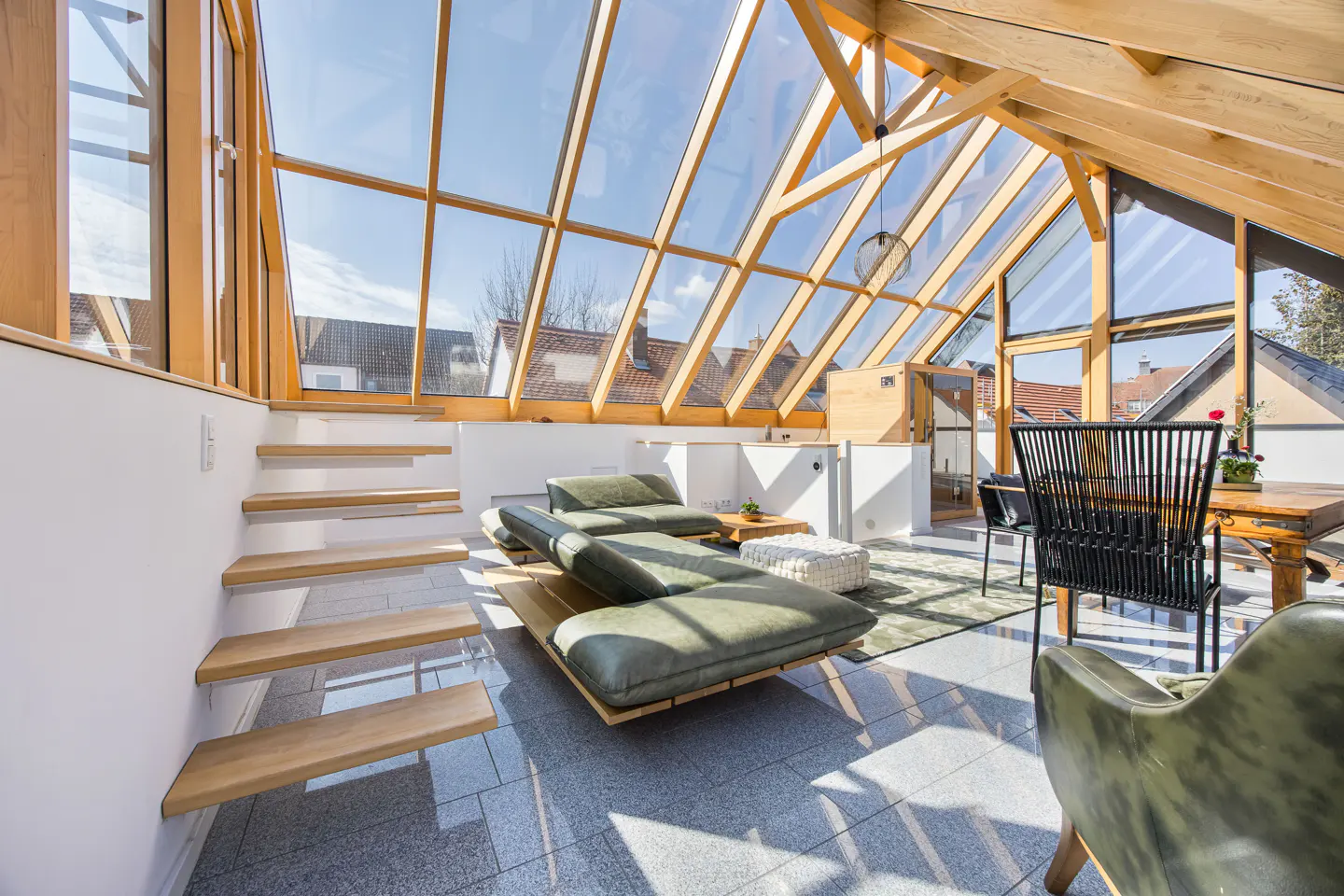 Bright sunroom with a glass ceiling, wooden beams, and gray tile floor. A green chaise lounge and wooden stairs add to the modern design.