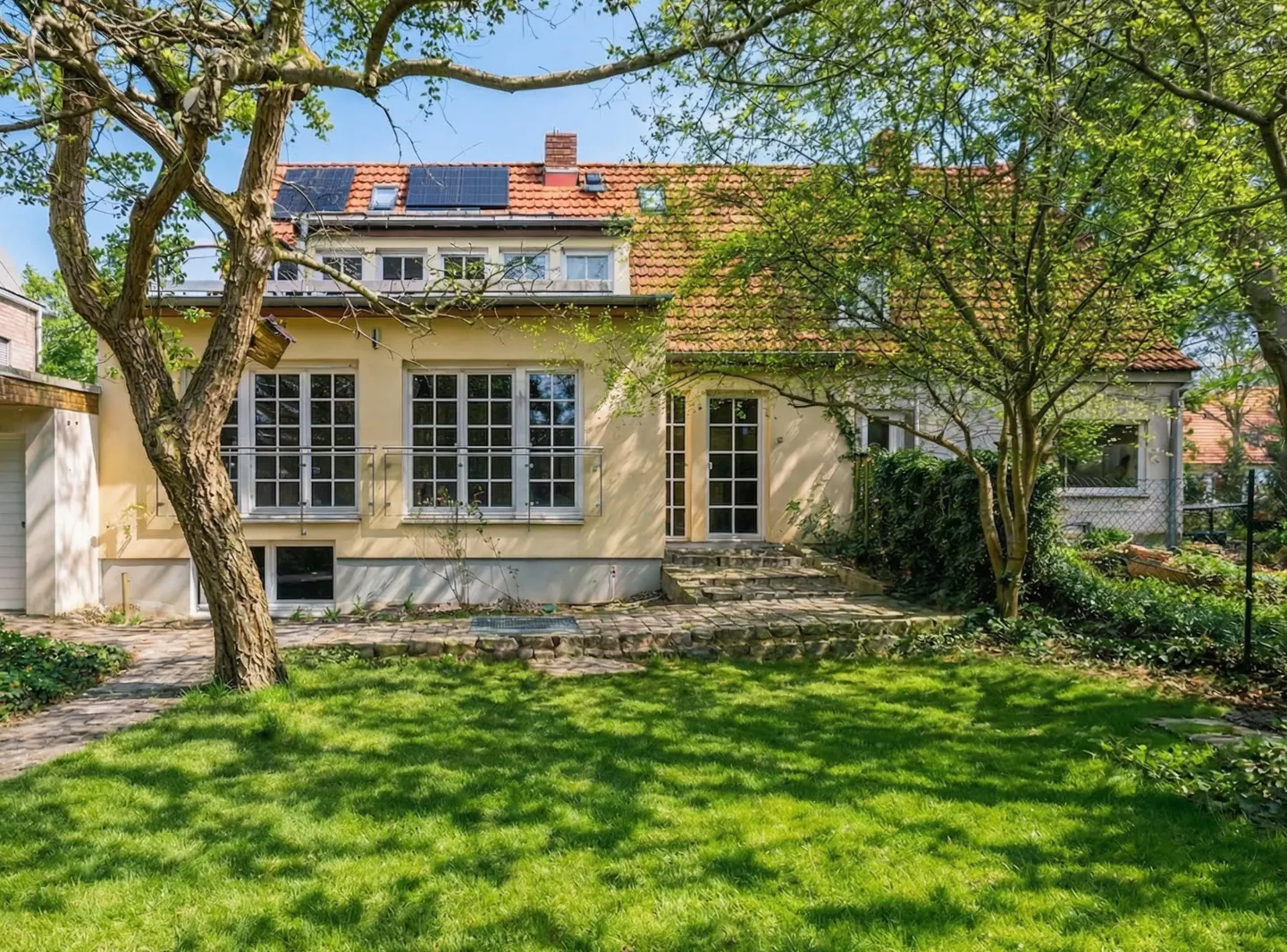 Back view of a yellow house with a red tile roof, solar panels, and a green lawn.