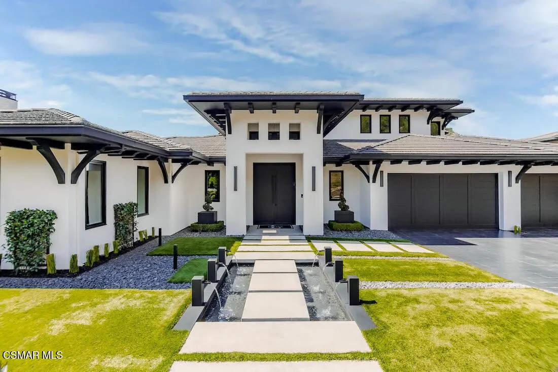 Modern white house with black trim, a gray roof, and a water feature leading to the front door.