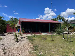 A single-story red house with a red roof and green pillars, surrounded by a yard with grass and gravel.