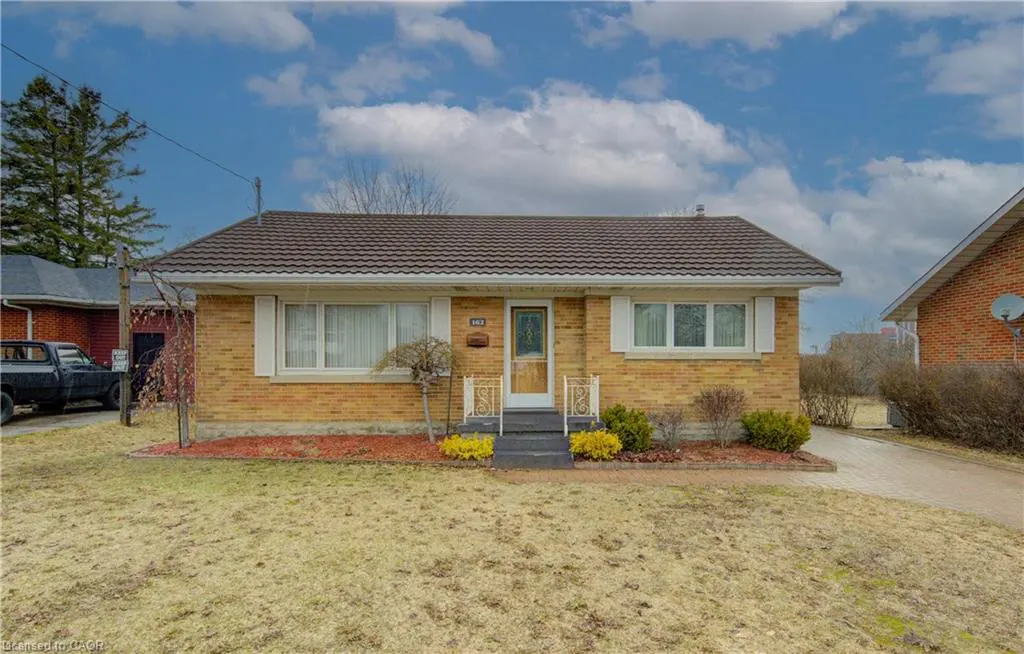 A single-story yellow brick house with a brown roof, white trim, and a small front yard.