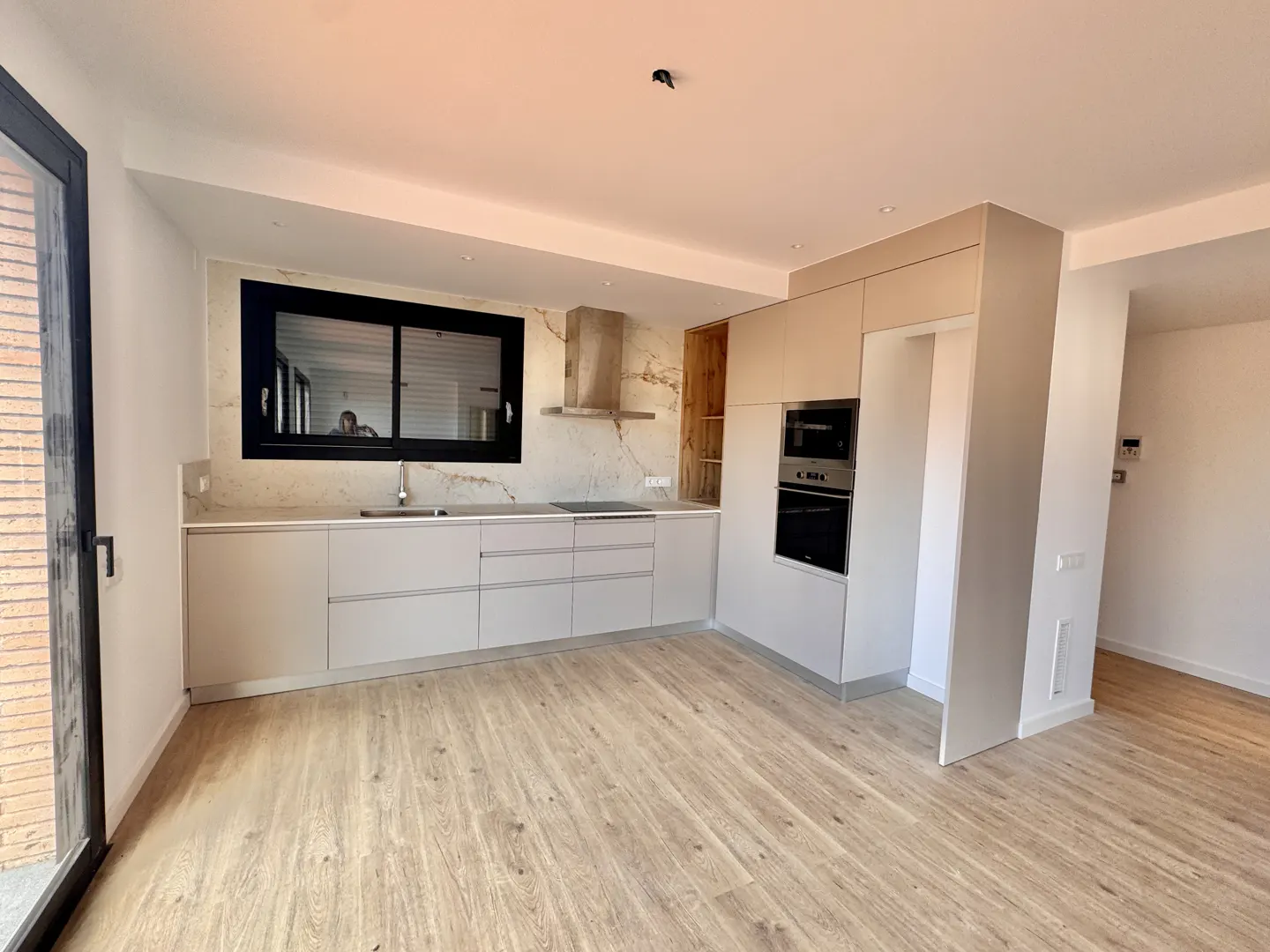 Bright, modern kitchen with light wood floors, white cabinets, black window frame, and stainless steel appliances.