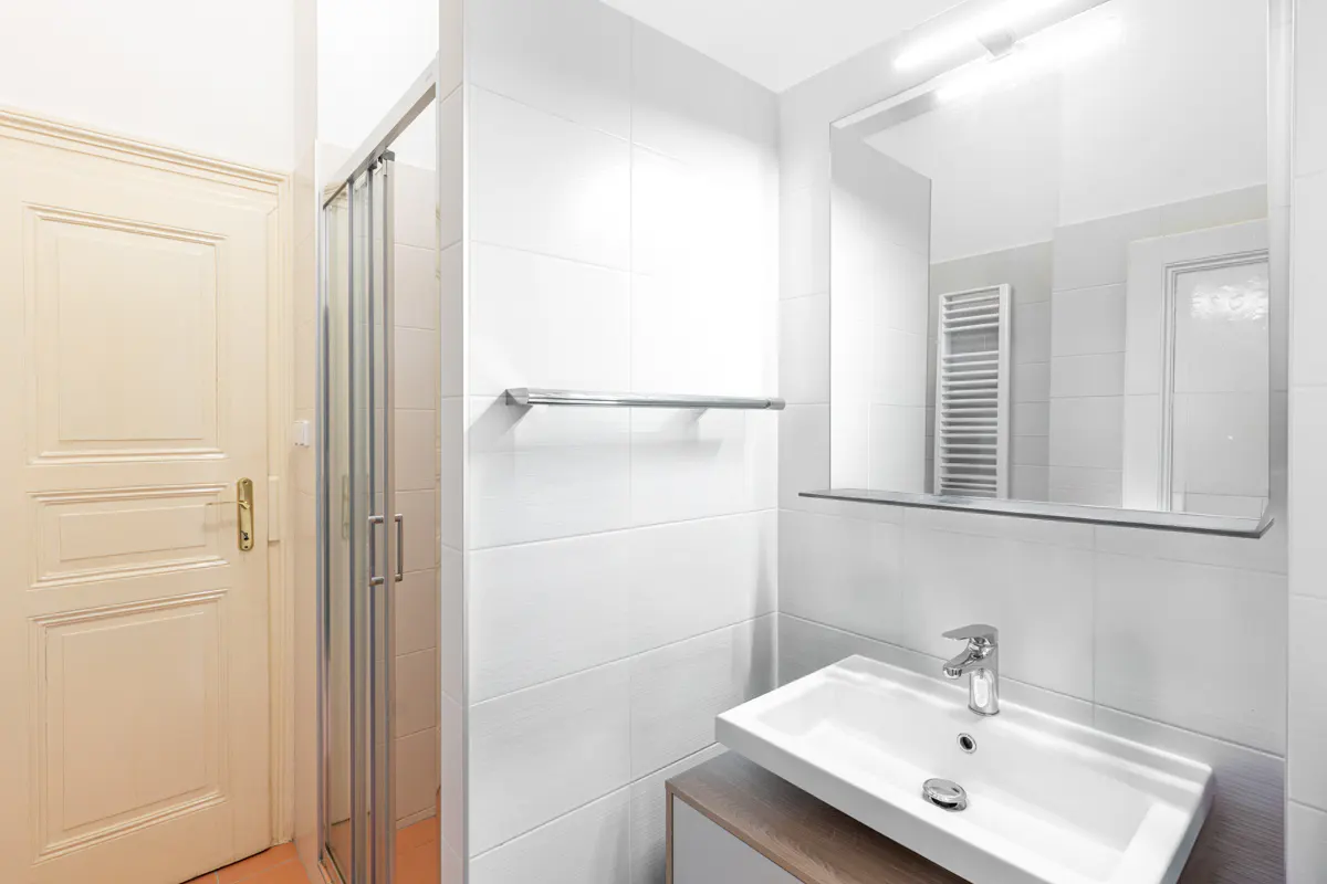 Modern white bathroom with a glass shower stall, a vanity sink, a large mirror, and a cream-colored paneled door.