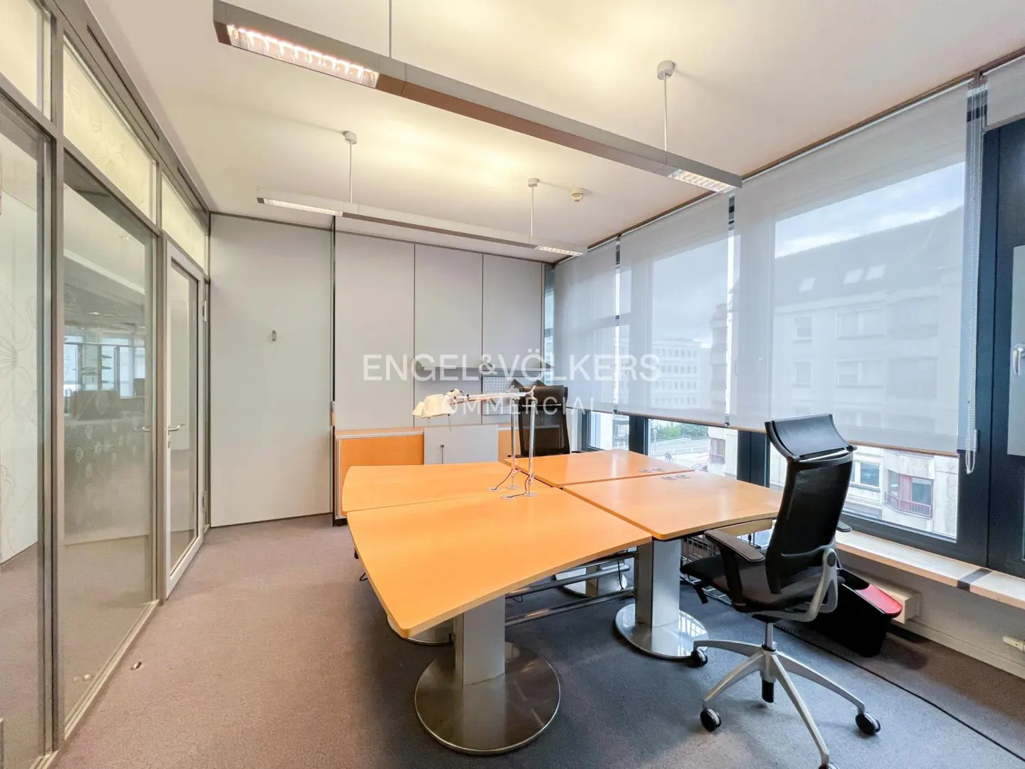 Bright office space with a large wooden table, black chairs, and floor-to-ceiling windows with white blinds.