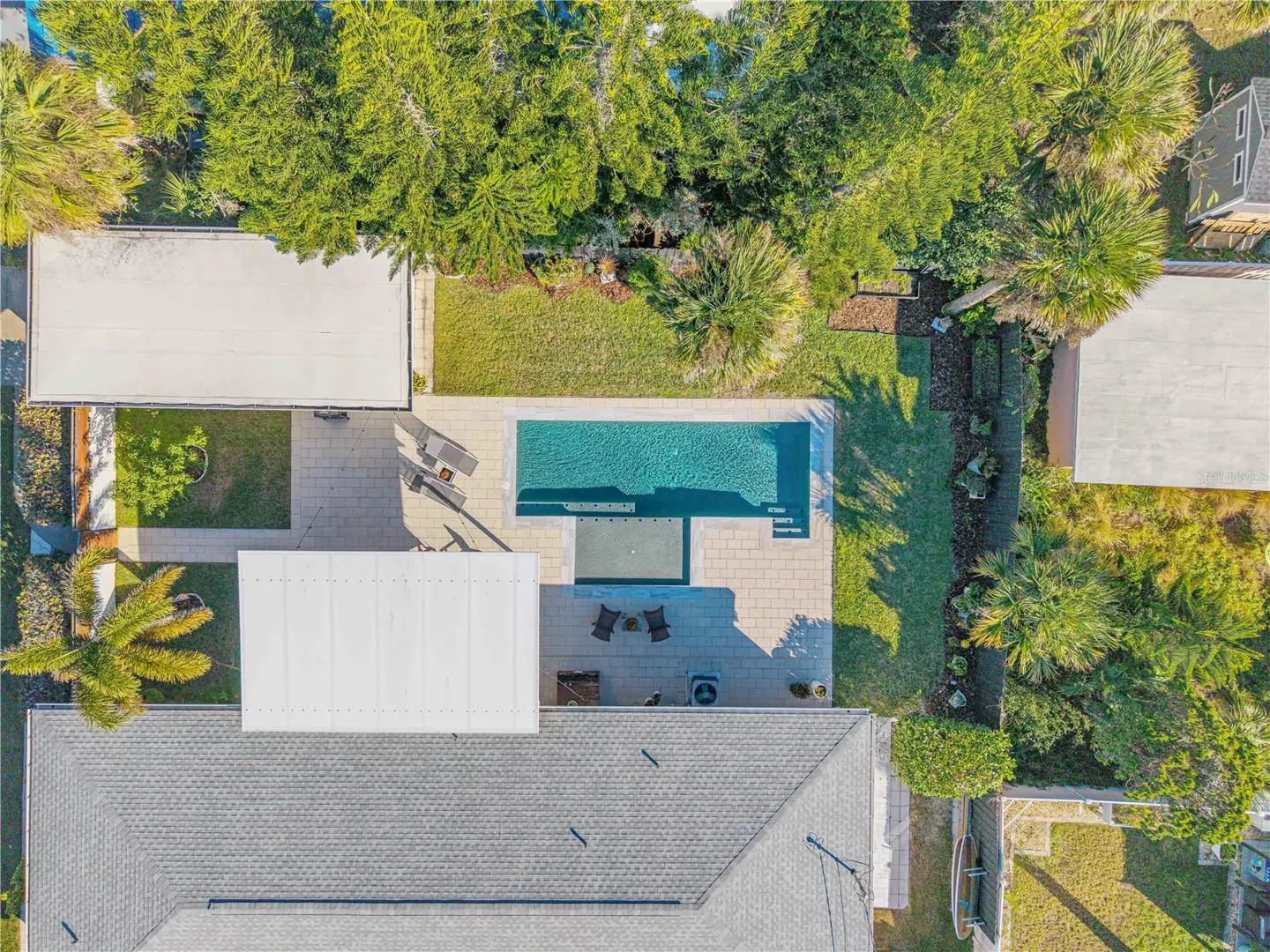 Aerial view of a house with a gray roof, a pool, a patio, and green trees.