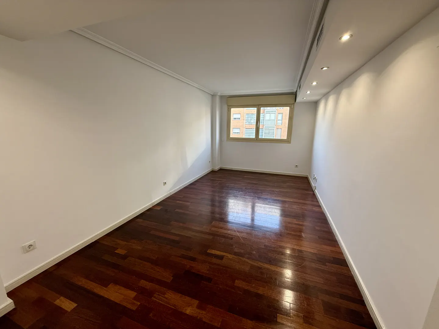 Bright, empty room with dark wood floors and white walls. A window lets in natural light.