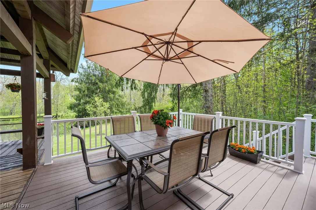 Outdoor patio with table, chairs, and umbrella. White railing surrounds the deck, overlooking a green, wooded area.