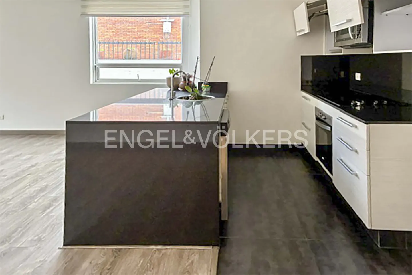 A modern kitchen with a dark island, white cabinets, and stainless steel appliances. A window overlooks a brick building.