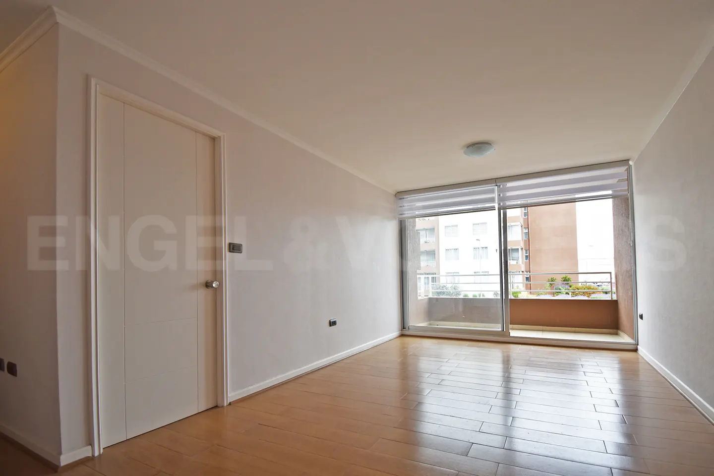Empty room with wood floors, white walls, and a sliding glass door to a balcony. A white door is on the left.