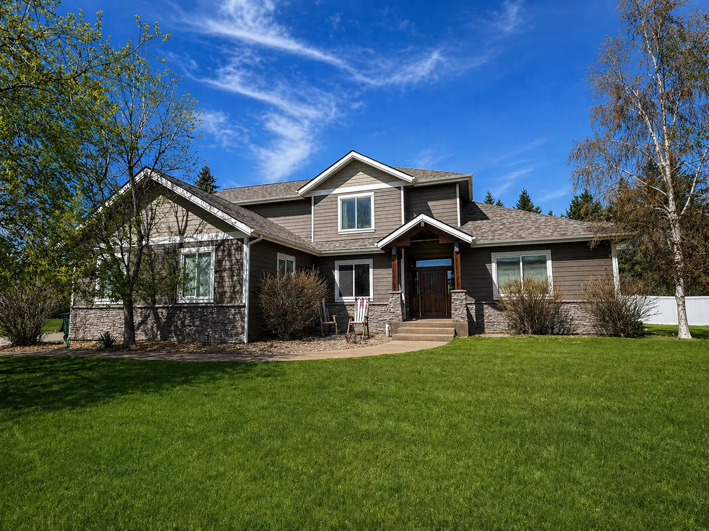 Two-story house with brown siding, stone accents, and a well-manicured green lawn under a blue sky.