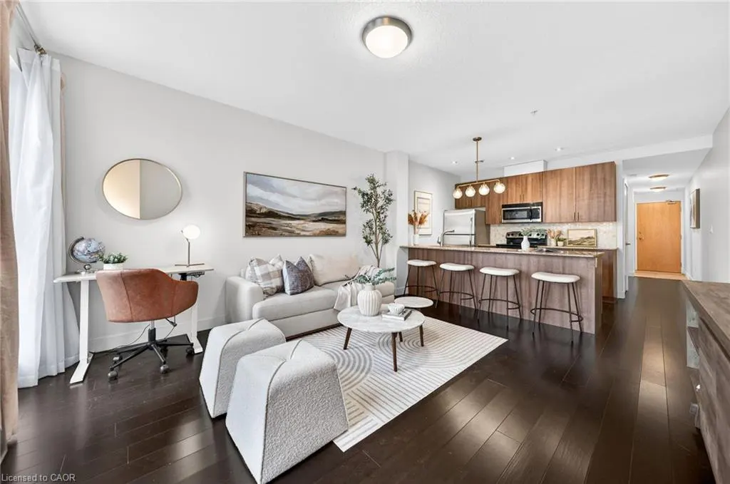 Bright, open-concept living space with a desk, sofa, kitchen island with stools, and dark wood floors.