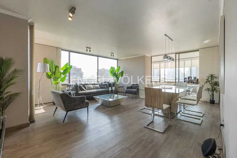 Bright, open-plan living and dining area with wood floors, large windows, and city views. Gray sofa and chairs, glass table, and modern dining set.