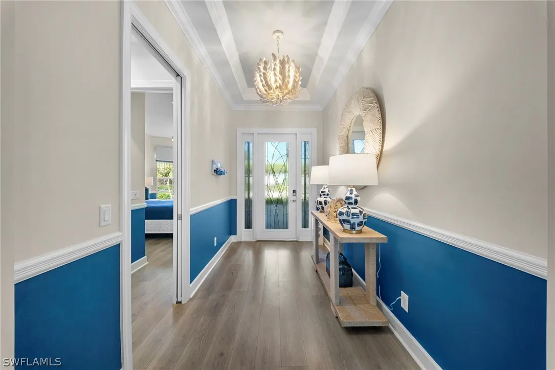 Entryway with blue wainscoting, light wood floors, and a console table with lamps and decor. A white chandelier hangs from the ceiling.