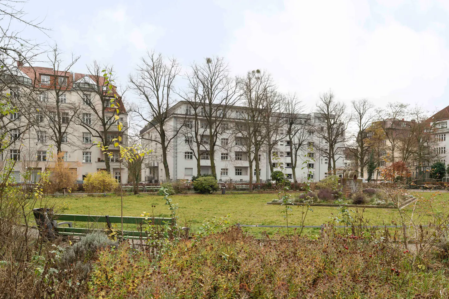 Apartment buildings surround a green space with trees, benches, and plants on an overcast day.